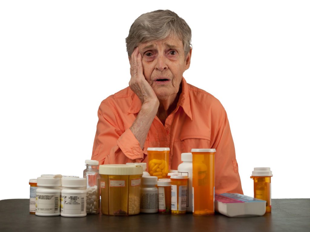An elderly woman with medications looking overwhelmed